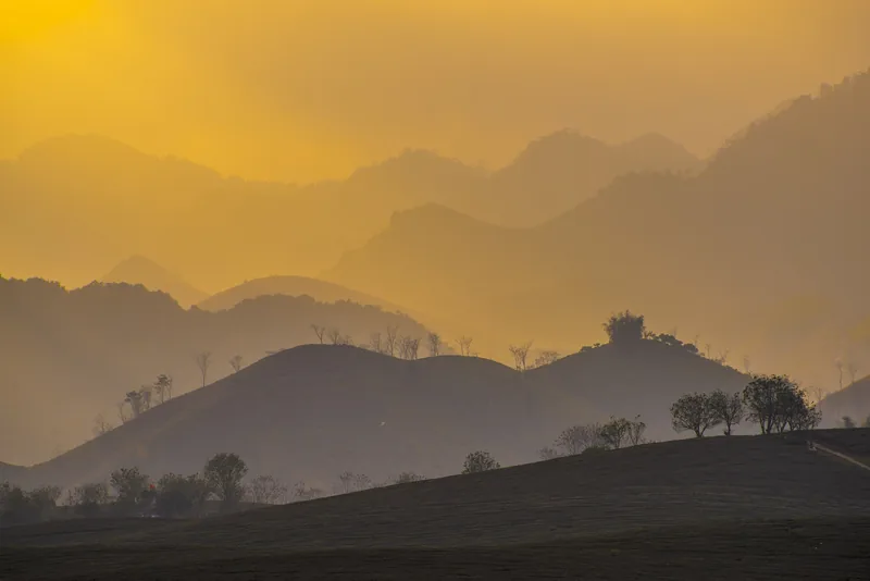 Layered mountain ridges fade into golden haze at sunrise in Moc Chau, Vietnam.