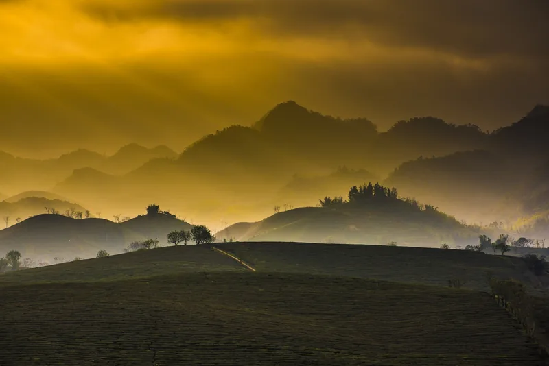 Golden sunrise light filters through layered misty hills and mountains in Moc Chau, Vietnam.