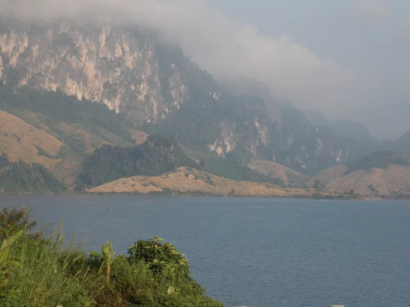 Limestone cliffs shrouded in mist rise above the calm waters of Son La Lake in Quynh Nhai, Vietnam.