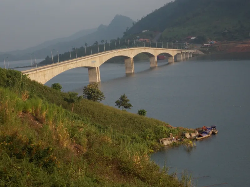 An arched concrete bridge spans the calm waters of Son La Lake amid green hills in Quynh Nhai, Son La.