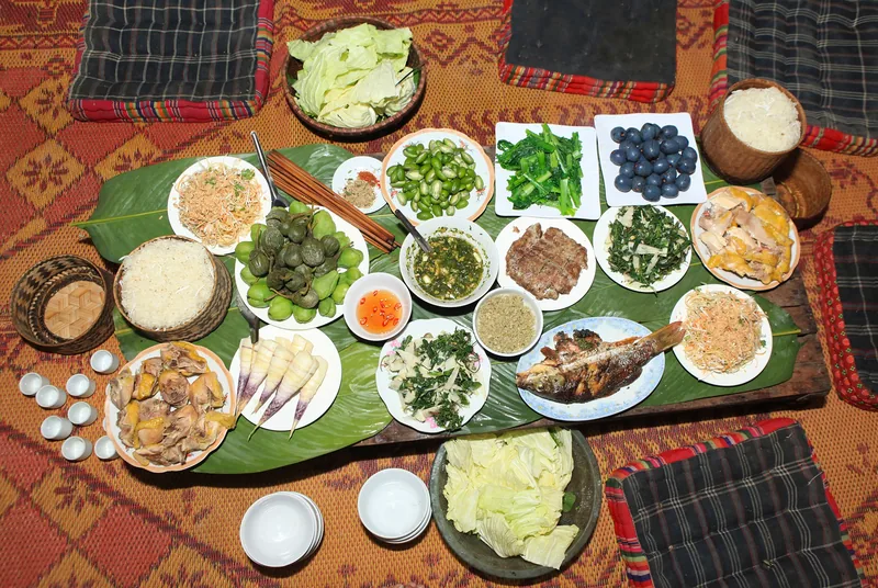 A traditional Thai feast in Son La with sticky rice, grilled fish, herbs and vegetables laid out on banana leaves.