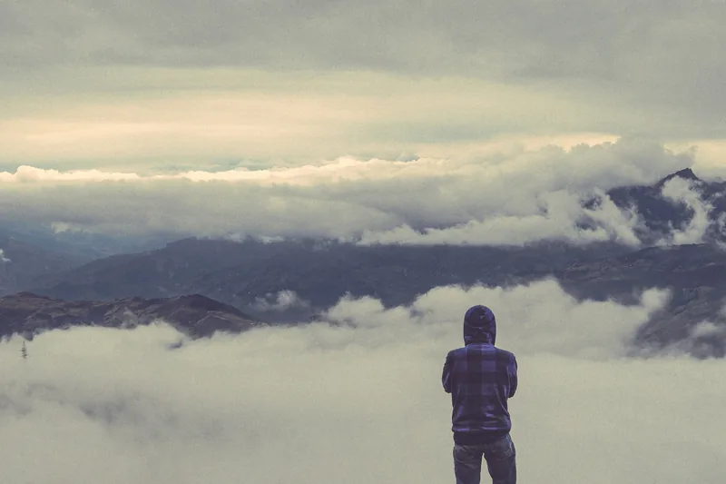 A hooded traveler stands on a ridge above a vast sea of clouds in Ta Xua, Son La.