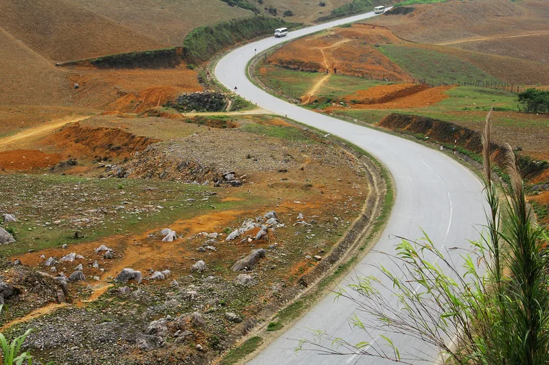A winding mountain road curves through the barren, reddish hills near Moc Chau, Son La.